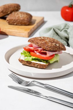 Prosciutto, peynir, domates, marul ve sosla birlikte sabah gölgesi, peçete ve çatalla yapılmış tahıllı sandviç. Sağlıklı ve diyet kahvaltı kavramı. 