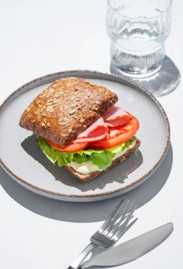 Prosciutto, domates, marul ve sostan yapılmış tahıllı sandviçle mavi zemin üzerinde bir bardak su. Kafe reklamları veya afişler için sağlıklı kahvaltı konsepti. Boşluğu kopyala.