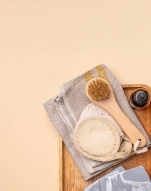 Cilt bakımı ürünleri ve aletler, serum şişesi, fırça ve havlu da dahil olmak üzere bej arka plandaki ahşap bir tepsiye yerleştirilmiş. Güzellik ve sağlık konsepti. Üst görünüm ve kopyalama alanı.