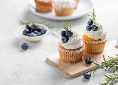 Krem peynirli kekler, taze yaban mersini ve ahşap tahtada biberiye, yakın plan çekimde. Lezzetli ev yapımı tatlı ya da tatil pişirme kavramı. Boşluğu kopyala.