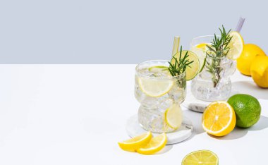 Limon, limon, biberiye ve buzlu iki bardak taze limonata. Beyaz gri arka planda Citrus kokteyli mojito. Bar menüsü reklamları veya afişler için yaz modasına uygun içecek konsepti. Boşluğu kopyala.