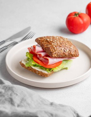 Jambonlu, peynirli, domatesli, salatalı ve soslu, peçete ve çatallı tahıllı sandviç. Sağlıklı ve diyet kahvaltı konsepti. Boşluğu kopyala.