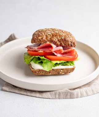 Jambonlu, peynirli, domatesli, marullu ve soslu tahıllı sandviç. Arka planda hafif bir tabakta. Sağlıklı ve diyet kahvaltı konsepti. Ön görünüm, boşluğu kopyala.