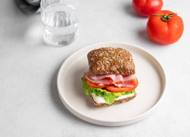 Jambonlu, peynirli, domatesli, marullu ve soslu tahıllı sandviç hafif bir zemin üzerinde bir bardak suyla. Sağlıklı ve diyet kahvaltı konsepti. Üst görünüm, alanı kopyala.