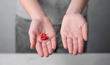 Bir çocuk kırmızı bir küpü açık avucunda tutar, diğeri boştur, tarafsız bir arkaplanda, karar vermeyi ya da şansı sembolize eder. Kumar konsepti.