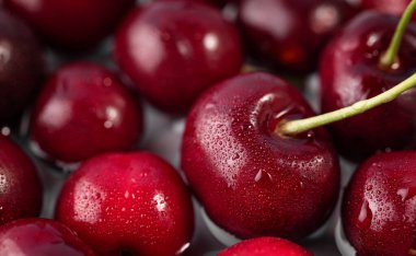 Su damlacıklarıyla kaplı taze kırmızı kirazlar, yakın plan fotoğraf tarzı, koyu arkaplanda. Tazelik ve sağlıklı beslenme kavramı bayrak ya da yiyecek reklamı içindir. Üst görünüm.