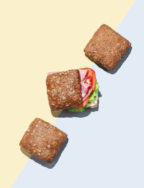 Jambonlu, marullu, domatesli ve soslu taze sandviç, sarı mavi arka planda tam tahıllı ekmek. Reklam afişi menüsü için sağlıklı beslenme kavramı. Üst görünüm, alanı kopyala.