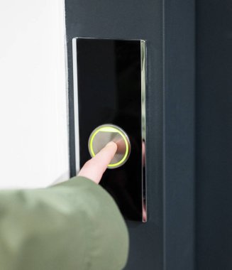 Pürüzsüz siyah panel, minimalist gerçek kapalı ortam, erişim konsepti üzerinde kişi parmak ışıklı kapı zili düğmesine yakın.