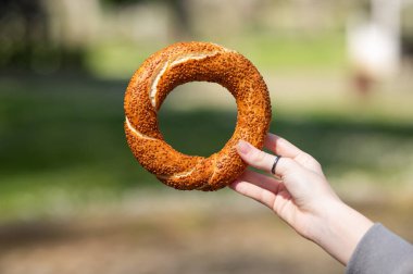 Güneşli bir günde bulanık parka karşı susamlı ekmek tutmak geleneksel sokak yemeği kültürünü sembolize ediyor. İstanbul, Türkiye
