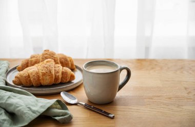 Bir bardak sütlü kahve ve ahşap bir masanın üzerinde cam zemininde peçeteyle taze kruvasan. Sabahları sağlıklı kahvaltı kavramı. Boşluğu kopyala.