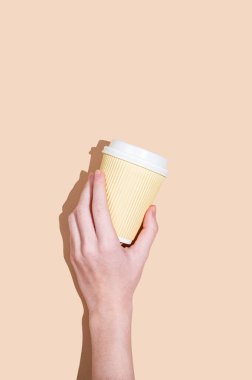 Sarı arka planda gölgeli kahve ile el ele tutuşan kağıt bardak. Kafe menüsü reklamları ve hızlı kahvaltı konsepti için yaratıcı bir model. Üst görünüm ve kopyalama alanı.