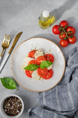 Domatesli Caprese salatası, mozzarella ve açık arkaplanda taze sebze ve güneş ışığında zeytinyağı bulunan fesleğen. Sağlıklı Akdeniz mutfağı konsepti. Üst görünüm.