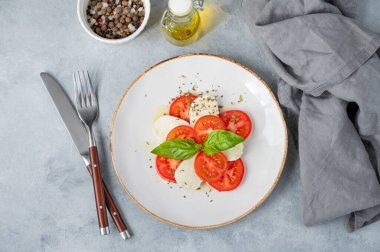 Dilimlenmiş domatesli Caprese salatası, mozzarella ve arka planda hafif bir tabakta taze sebze ve zeytinyağlı fesleğen. Sağlıklı Akdeniz mutfağı konsepti. Üst görünüm ve kopyalama alanı.