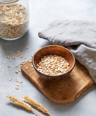 Tahtadaki yulaf gevrekleri peçete, buğday ve cam kavanozla birlikte gri desenli arka planda. Sağlıklı beslenme ve sağlıklı diyet kahvaltı konsepti. Üst görünüm ve kopyalama alanı.