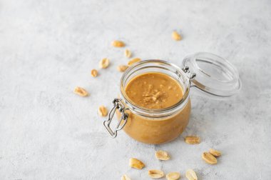 Gri arka planda kremalı fıstık ezmeli cam kavanoz. Kavrulmuş fındık ve doğal ışık. Doğal ev yapımı fıstık ezmesi konsepti. Üst görünüm ve kopyalama alanı.