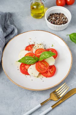 Dilimlenmiş domatesli Caprese salatası, mozzarella ve arka planda hafif bir tabakta taze sebze ve zeytinyağlı fesleğen. Sağlıklı Akdeniz mutfağı kavramı.