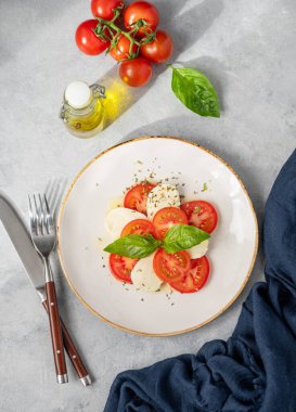 Domatesli Caprese salatası, mozzarella ve açık arkaplanda taze sebze ve güneş ışığında zeytinyağı bulunan fesleğen. Sağlıklı Akdeniz mutfağı konsepti. Üst görünüm.