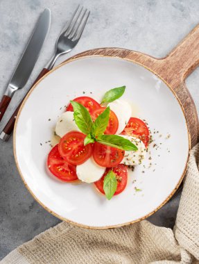 Dilimlenmiş domatesli Caprese salatası, mozzarella ve ahşap bir tahtada peçeteli fesleğen. Sağlıklı Akdeniz mutfağı konsepti. Üst görünüm.