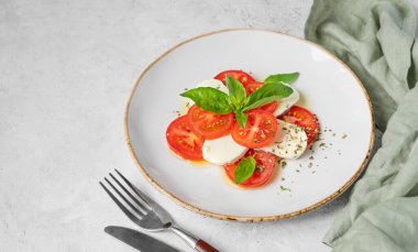 Domatesli Caprese salatası, mozzarella ve doğal ışıkta peçeteli beyaz arka planda bir tabakta fesleğen. Sağlıklı Akdeniz mutfağı konsepti. Boşluğu kopyala.