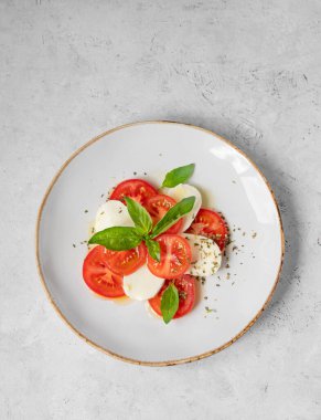 Domatesli Caprese salatası, mozzarella ve doğal ışıkta beyaz arka planda bir tabakta fesleğen. Sağlıklı Akdeniz mutfağı konsepti. Üst görünüm ve kopyalama alanı.