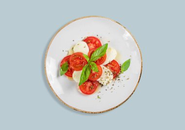 Domatesli taze Caprese salatası, mozzarella ve mavi arka planda fesleğen. Bir kafe veya restoran menüsü için reklam afişi. Sağlıklı beslenme konsepti. Üst görünüm, alanı kopyala.