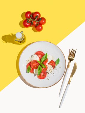 Domatesli taze Caprese salatası, mozzarella ve parlak gölgeli beyaz sarı arka planda fesleğen. Bir kafe veya restoran menüsü için reklam afişi. Sağlıklı beslenme konsepti. Üst görünüm.