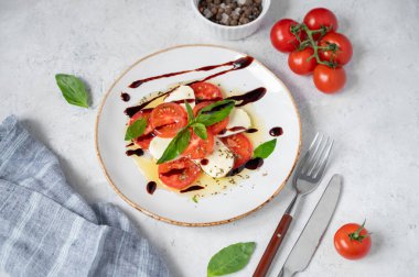 Dilimlenmiş domatesli taze Caprese salatası, mozzarella peyniri, fesleğen yaprağı ve açık arkaplanda taze sebze ve baharatlı balzamik cila. Sağlıklı beslenme konsepti. Üst görünüm.