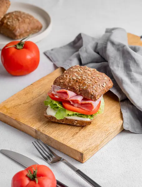 Jambonlu, peynirli, domatesli tahıllı sandviç, ahşap bir tahtada salata ve sos peçete ve çatalla birlikte. Sağlıklı ve diyet kahvaltı konsepti. Boşluğu kopyala.