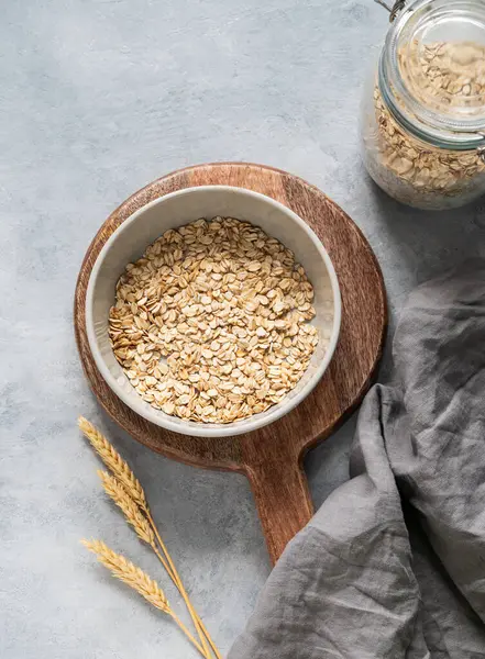 Tahtadaki yulaf gevrekleri peçete, buğday ve cam kavanozla birlikte gri desenli arka planda. Sağlıklı beslenme ve sağlıklı diyet kahvaltı konsepti. Üst görünüm ve kopyalama alanı.