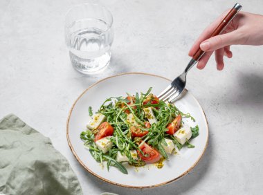 Kiraz domatesli roka salatası, mozzarella ve bir bardak suyla desenli hafif arkaplanda pesto sosu. Taze ve sağlıklı Akdeniz mutfağı kavramı. Üst görünüm.