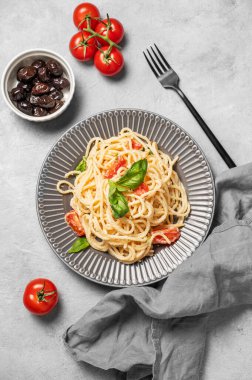 Kirazlı domatesli leziz kremalı spagetti, parmesan peyniri ve gri dokulu arka planda bir tabakta fesleğen. İtalyan ya da Akdeniz mutfağı konsepti. Üst görünüm.