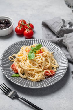 Kiraz domatesli kremalı spagetti, parmesan peyniri ve açık arkaplanda bir tabakta fesleğen ve bir bardak su ve zeytin. İtalyan ya da Akdeniz mutfağı kavramı. 