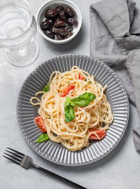Kiraz domatesli kremalı spagetti, parmesan peyniri ve açık arkaplanda bir tabakta fesleğen ve bir bardak su ve zeytin. İtalyan ya da Akdeniz mutfağı konsepti. Üst görünüm.