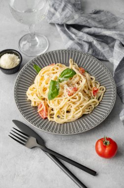 Kiraz domatesli kremalı spagetti, parmesan peyniri ve bir tabak açık arkaplanda bir bardak suyla fesleğen. İtalyan ya da Akdeniz mutfağı konsepti. Üst görünüm.