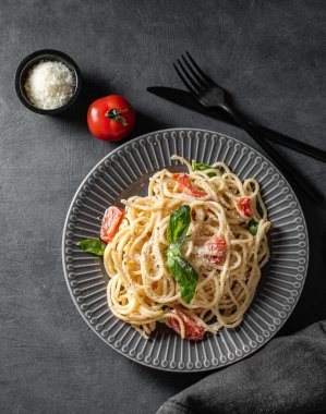 Çeri domatesli kremalı spagetti, koyu arkaplanda parmesan peyniri ve fesleğen. İtalyan ya da Akdeniz mutfağı konsepti. Üst görünüm ve kopyalama alanı.