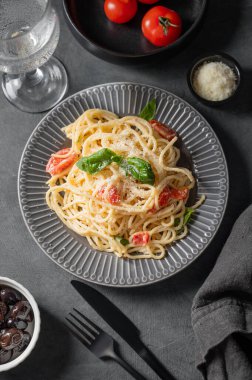 Çeri domatesli kremalı spagetti, parmesan peyniri ve fesleğen ile koyu bir zemin üzerinde bir bardak su ve zeytin. İtalyan ya da Akdeniz mutfağı konsepti. Üst görünüm.