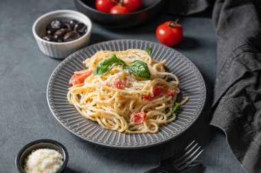 Çeri domatesli kremalı spagetti, parmesan peyniri ve koyu arkaplanda zeytinli fesleğen. İtalyan ya da Akdeniz mutfağı kavramı. 