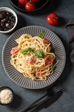Çeri domatesli kremalı spagetti, parmesan peyniri ve koyu arkaplanda zeytinli fesleğen. İtalyan ya da Akdeniz mutfağı konsepti. Üst görünüm.