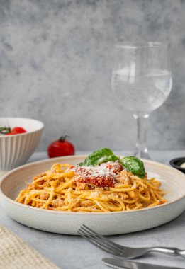 Domates soslu spagetti bolonez, fesleğen ve parmesan peyniri gri bir arka planda bir bardak suyla. İtalyan ya da Akdeniz diyet mutfağı kavramı. Boşluğu kopyala.