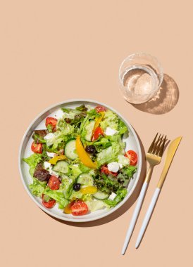 Sebze salatası, marul, sebze, zeytin ve bej arka planda beyaz peynir, bir bardak su ve çatal bıçakla. Afiş reklamcılığı veya menü düzeni için taze ve doğal sağlıklı gıda konsepti. 