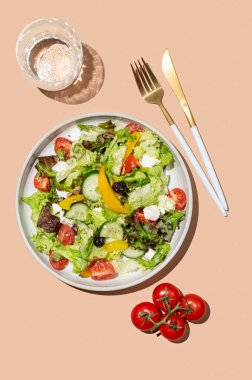 Sebze salatası, marul, sebze, zeytin ve bej arka planda beyaz peynir, bir bardak su ve çatal bıçakla. Afiş reklamcılığı veya menü düzeni için taze ve doğal sağlıklı gıda konsepti. 