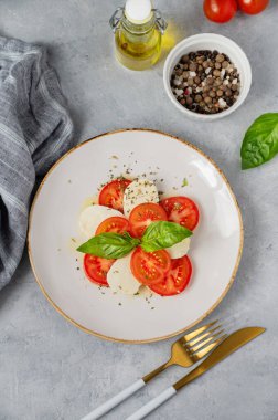 Dilimlenmiş domatesli Caprese salatası, mozzarella ve doğal ışıkta peçeteli beyaz arka planda bir tabakta fesleğen. Sağlıklı Akdeniz mutfağı konsepti. Üst görünüm ve kopyalama alanı.