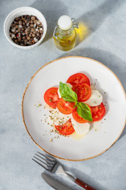 Dilimlenmiş domatesli Caprese salatası, mozzarella ve doğal ışıkta peçeteli beyaz arka planda bir tabakta fesleğen. Sağlıklı Akdeniz mutfağı konsepti. Üst görünüm ve kopyalama alanı.