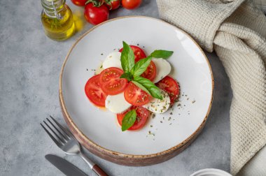 Dilimlenmiş domatesli Caprese salatası, mozzarella ve doğal ışıkta peçeteli beyaz arka planda bir tabakta fesleğen. Sağlıklı Akdeniz mutfağı konsepti. Üst görünüm ve kopyalama alanı.