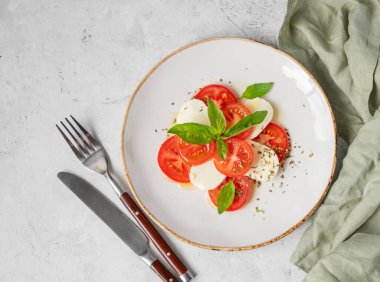 Domatesli Caprese salatası, mozzarella ve doğal ışıkta peçeteli beyaz arka planda bir tabakta fesleğen. Sağlıklı Akdeniz mutfağı konsepti. Üst görünüm ve kopyalama alanı.