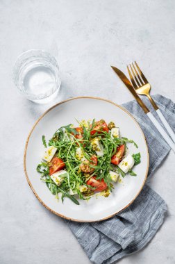 Kiraz domatesli sağlıklı roka salatası, mozzarella ve hafif dokulu arka planda bir tabakta pesto sosu, bir bardak suyla. Taze ve sağlıklı Akdeniz gıda konsepti. Üst görünüm 