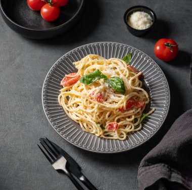 Çeri domatesli kremalı spagetti, koyu arkaplanda parmesan peyniri ve fesleğen. İtalyan ya da Akdeniz mutfağı konsepti. Üst görünüm ve kopyalama alanı.