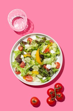 Sebzeli salata, marul, sebze, zeytin ve bir bardak suyla pembe arka planda beyaz peynir. Afiş reklamı ya da menü düzeni için taze ve doğal sağlıklı gıda konsepti. Üst görünüm.
