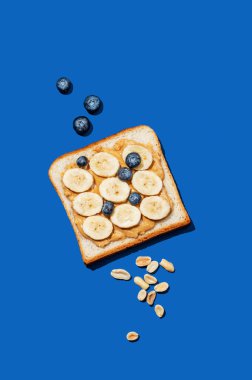 Fıstık ezmeli, muzlu, yabanmersinli ve fındıklı tost koyu mavi arka planda. Reklam menüsü ya da afiş için tatlı ve sağlıklı atıştırmalıklar kavramı. Üst görünüm ve kopyalama alanı.