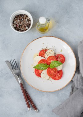 Dilimlenmiş domatesli Caprese salatası, mozzarella ve arka planda hafif bir tabakta zeytinyağı ve baharatlı fesleğen. Sağlıklı Akdeniz mutfağı konsepti. Üst görünüm ve kopyalama alanı.